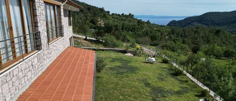 A stone building with a tiled terrace overlooking a lush green landscape and a body of water.