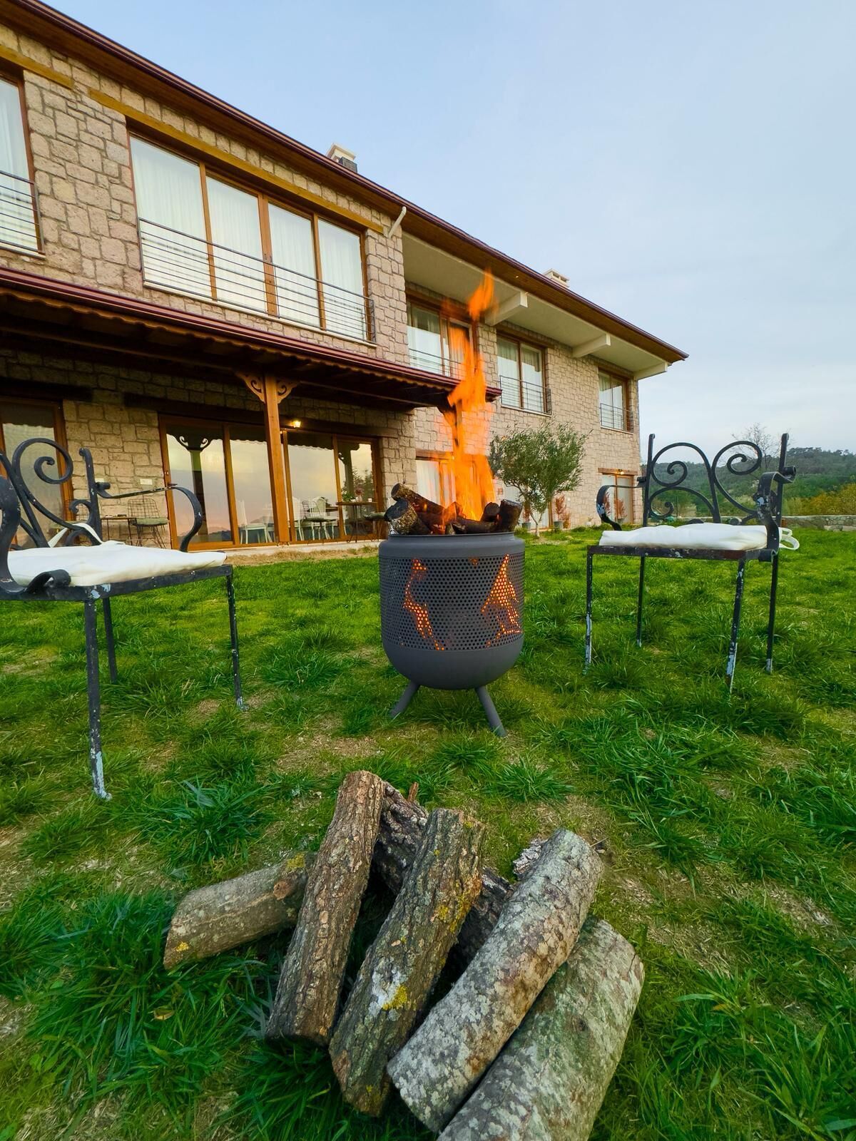 A stone building with a fire pit in the foreground and two outdoor seating areas.