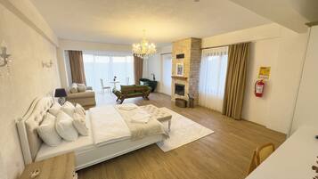 Une chambre spacieuse avec un grand lit, un coin salon avec un canapé et des fauteuils, une cheminée et une vue sur l’extérieur.