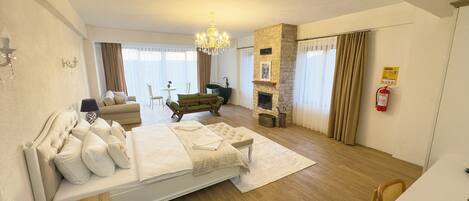 Ein geräumiges Schlafzimmer mit einem großen Bett, einer Sitzecke mit Sofa und Sesseln, einem Kamin und Blick ins Freie.