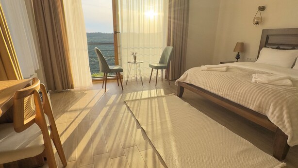 Een hotelkamer met een groot bed, een bureau met stoel, een kleine tafel met stoelen en uitzicht op zee.
