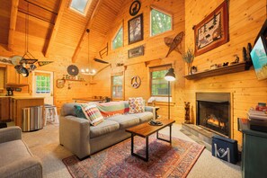 Interior acogedor de una cabaña con chimenea, paredes de madera, un sofá y zona de comedor.