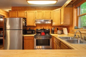 Una cocina con armarios de madera, electrodomésticos de acero inoxidable, un microondas, una estufa y un fregadero.