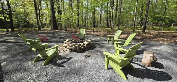 Un camping con sillas Adirondack verdes dispuestas alrededor de una fogata.