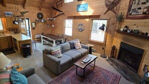 Interior acollidor d'una cabana amb zona de menjador, sofà, llar de foc i parets de fusta.