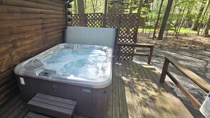 Jacuzzi en un pont de fusta amb escales que hi condueixen, tot voltat d'una tanca de fusta i arbres.