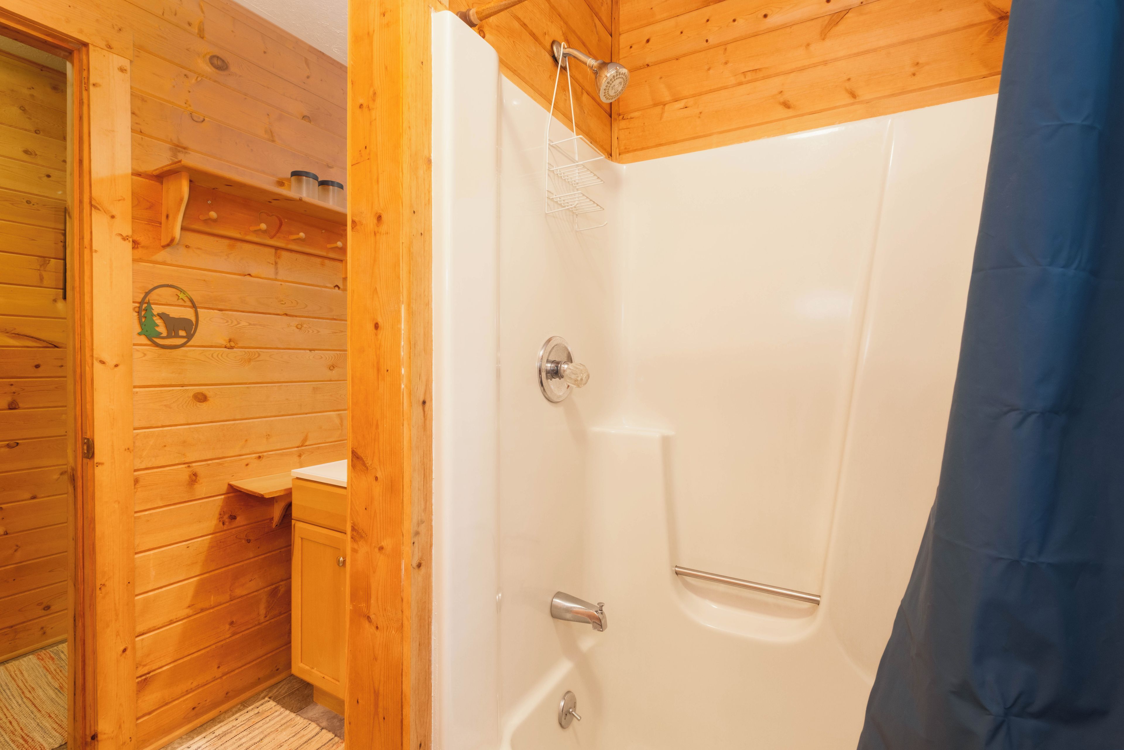 Bany d'una cabana de fusta amb dutxa, penjador de tovalloles i una petita estantella.