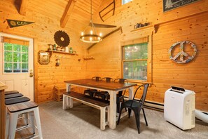 Un interior de madera con una mesa de comedor, sillas, un banco, un calentador y una ventana con vistas a árboles.