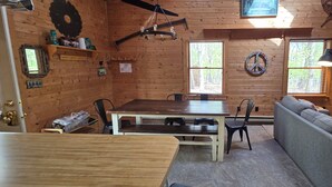 Interior acollidor d'una cabana, amb taula de dinar de fusta, cadires, sofà i una llar de foc.