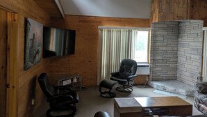 Una sala de estar acogedora con paredes de madera, chimenea, televisor y asientos cómodos.
