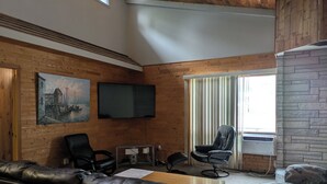 Una habitación moderna con paredes de madera, televisor de pantalla plana, mobiliario de cuero y chimenea de piedra.