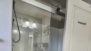 Une salle de bain avec une douche à parois de verre, une porte blanche portant l’inscription « Toilettes » et un porte-serviettes visible.