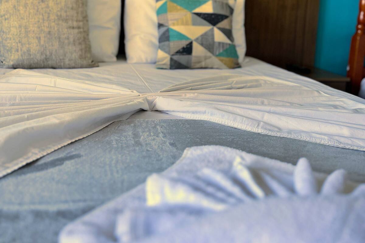 Una cama con ropa blanca y un cojín de estampado geométrico.