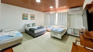A hotel room with two beds, a desk, a television, and a window with curtains. - POUSADA BELUGA (Buzios)