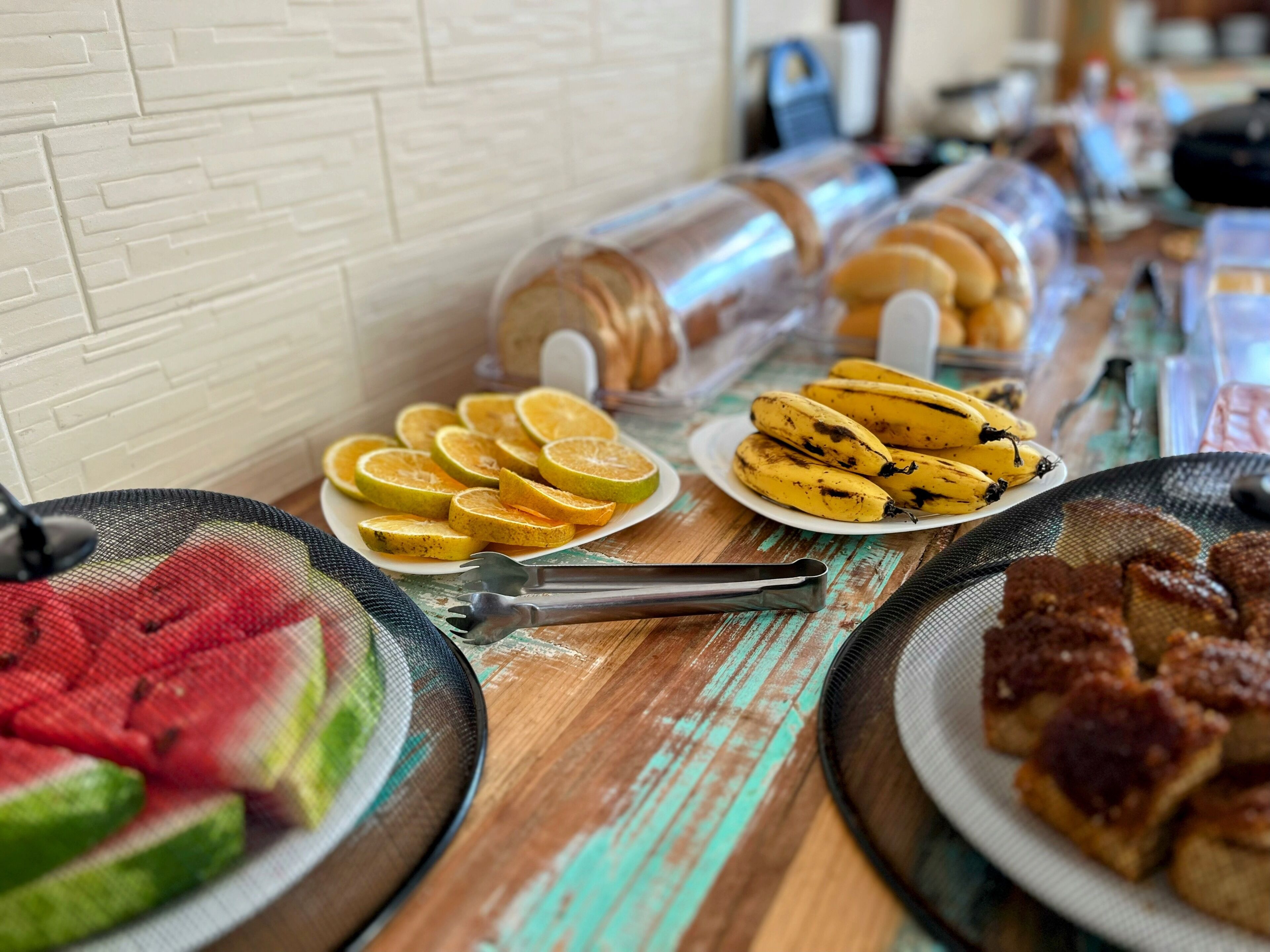 A breakfast buffet with sliced oranges, bananas, and various pastries on a wooden table.