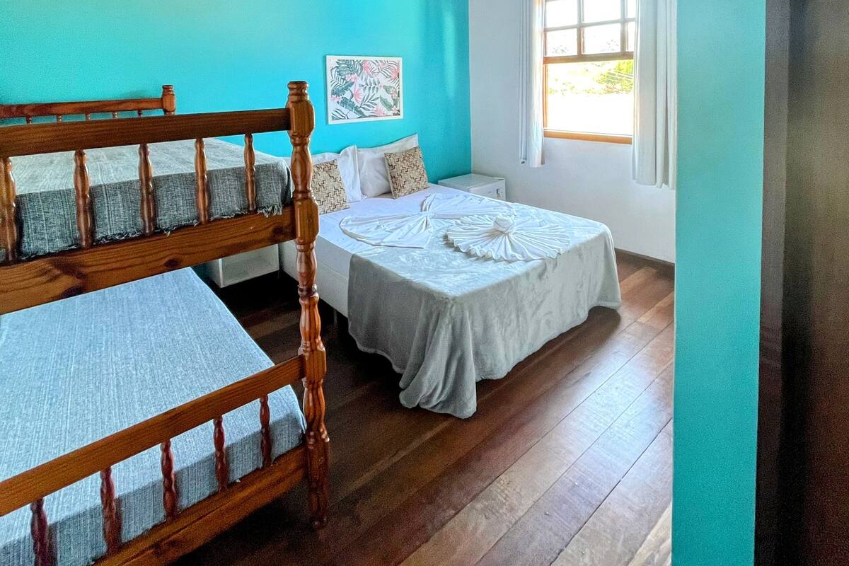 Una habitación con una cama de madera, una cama más pequeña, un ventilador de techo y una ventana con cortinas.