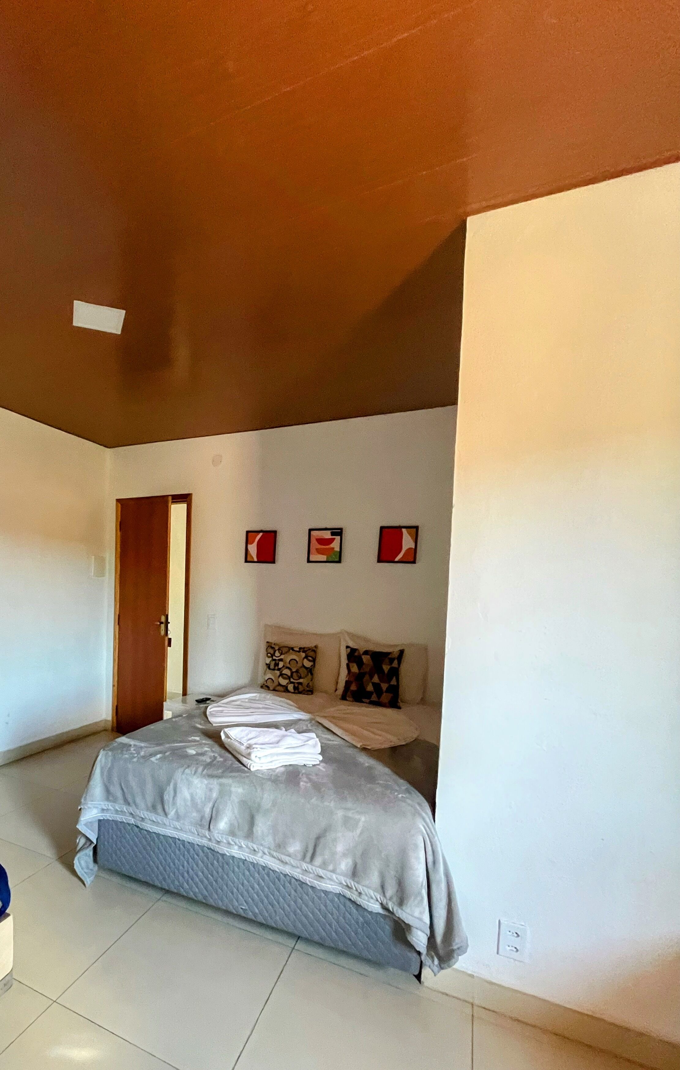 A bedroom with a bed, a door, and three wall-mounted pictures.