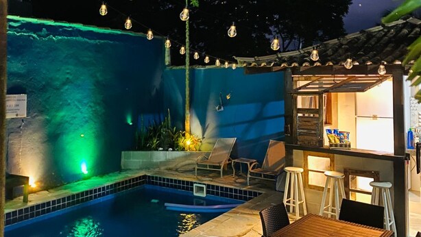A pool area with a tiled edge, lounge chairs, a bar area with stools, and a small waterfall feature. - POUSADA BELUGA (Buzios)