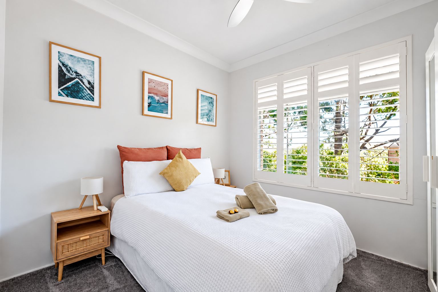 A hotel room with a bed, two bedside tables, a nightstand, and a window with blinds.