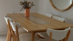 Un comedor con una mesa de madera y sillas blancas, una planta en maceta y cuadros en la pared.