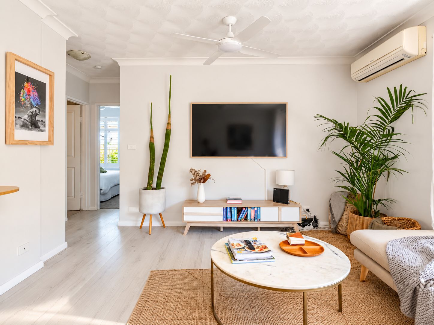 Ein modernes Wohnzimmer mit einem weißen Sofa, einem runden Couchtisch, einem Flachbildfernseher und einem Deckenventilator.