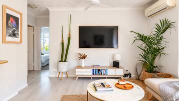 Ein modernes Wohnzimmer mit einem weißen Sofa, einem runden Couchtisch, einem Flachbildfernseher und einem Deckenventilator.
