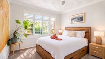 A bedroom with a wooden bed, a nightstand, a lamp, a potted plant, and a window with blinds.