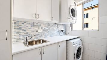 A modern kitchen with white cabinets, a stainless steel sink, a tiled backsplash, and a built-in washing machine.