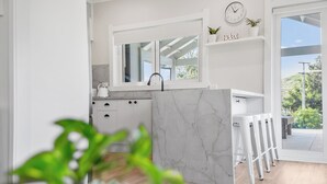 Une cuisine moderne avec des meubles blancs, un plan de travail en marbre et une grande fenêtre.