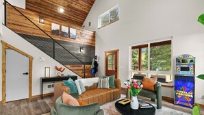 A spacious living area with a wooden staircase, a sofa set, a coffee table, and a large window offering a view of the outdoors.