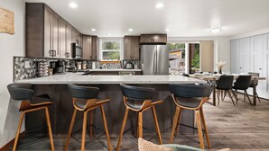 A modern kitchen with a central island, bar stools, and a dining area with chairs.