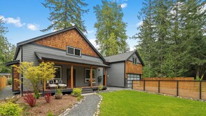 A modern house with a grey exterior, a wooden deck, and a well-maintained lawn.