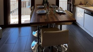 A dining area with a wooden table set for four, a kitchen with a sink and dishwasher, and a view through large sliding glass doors.