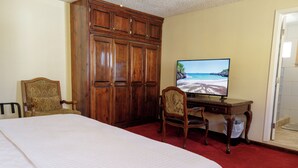 A bedroom with a large bed, a wooden wardrobe, a desk with a chair, and a television displaying a beach scene. - Cozy 1 king bed apartment in enjoyable Ensenada with pool, fitness room. (Ensenada)
