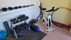 A home gym with a wall-mounted dumbbell rack, a stationary bike, and exercise mats. - Cozy 1 king bed apartment in enjoyable Ensenada with pool, fitness room. (Ensenada)