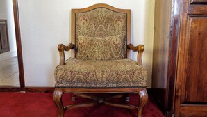 A vintage chair with a patterned upholstery, positioned on a red carpet in a room with wooden furniture. - Cozy 1 king bed apartment in enjoyable Ensenada with pool, fitness room. (Ensenada)