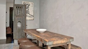 A rustic wooden table with a white bowl, accompanied by leather stools, in a room with a plain wall and a door leading to another space. - Charming 3-bedroom Modern Rustic Retreat on 1 acre (Keller)