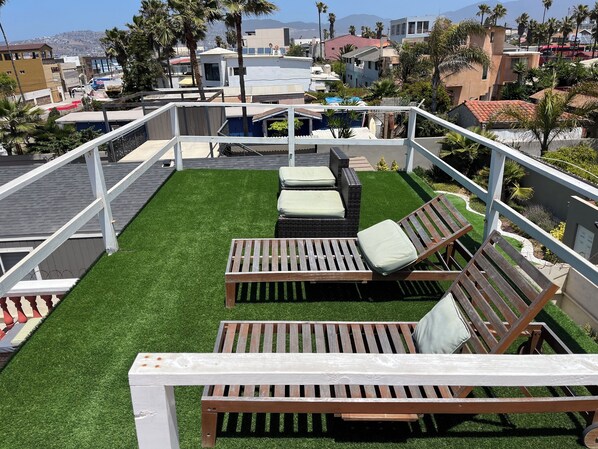 Una terraza en la azotea con césped artificial, dos sillones de madera y una barandilla blanca.