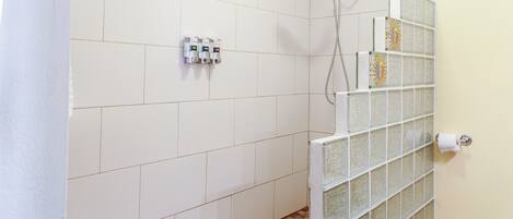 A bathroom with white tiled walls, a shower with a glass partition, and a toilet paper holder.