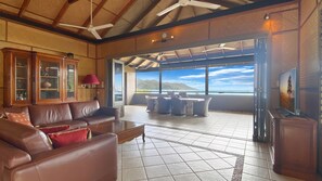 Relax in this inviting living area with a sofa, armchair, and coffee table, offering a view of the sea and distant hills through the large sliding glass door.