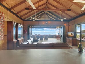A spacious room with a large window overlooking the sea, a seating area with a table, and a television on the wall. - Absolute Beachfront Master (Horseshoe Bay)