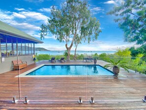 A swimming pool with a wooden deck, lounge chairs, and a view of the sea. - Absolute Beachfront Master (Horseshoe Bay)