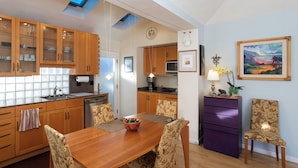 Una cocina moderna con armarios de madera, una mesa de comedor con sillas, un mueble de almacenamiento morado y un cuadro en la pared.