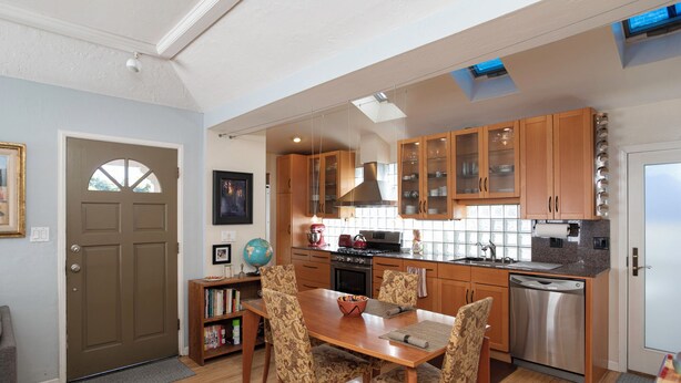 Una cocina moderna con armarios de madera, lavavajillas de acero inoxidable y un comedor con sillas estampadas y una mesa de madera.