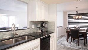 A modern kitchen with white cabinets, a black countertop, and a built-in dishwasher. - 1277 Belridge Apt14C-Monthly (Oceano)