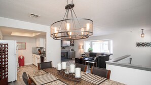 A dining area with a large table, chairs, and a chandelier. There is a kitchen in the background with cabinets and a countertop. - 1277 Belridge Apt14C-Monthly (Oceano)