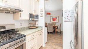 A kitchen with a stove, microwave, and refrigerator, wooden cabinets, and a dining area with chairs and a table. - 364 Harbor View (Pismo Beach)