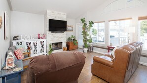 A living room with a fireplace, a television, and a large window with a view of the outdoors. - 364 Harbor View (Pismo Beach)