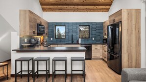 A modern kitchen with wooden cabinets, a central island with bar stools, a stainless steel refrigerator, and a blue backsplash.