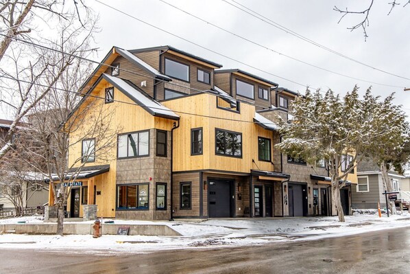A modern multi-story residential building with a mix of wood and stone exterior, large windows, and a visible fire hydrant on the street.